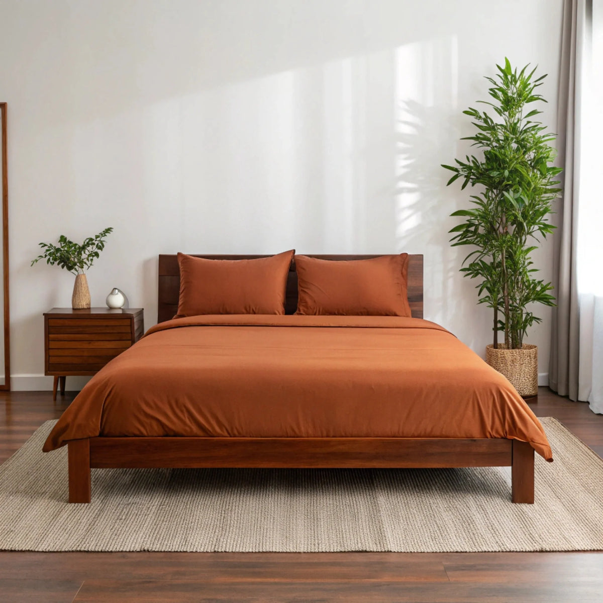 Copper-infused bamboo sheet set by Bamboo is Better, shown in a cozy bedroom with rust-colored sheets on a full bed.